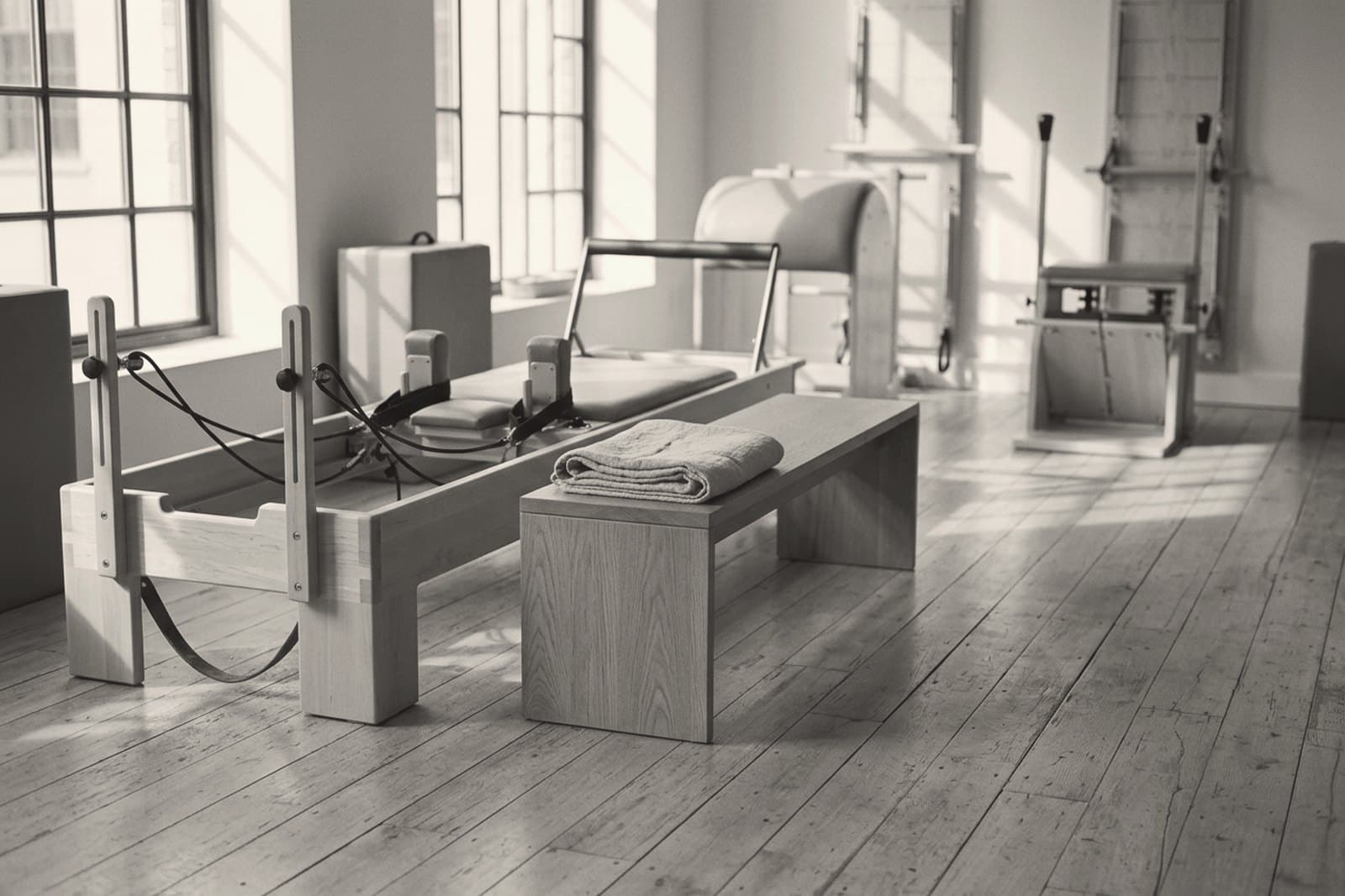 A small pilates studio mid-morning, equipment at rest and a folded towel on the bench